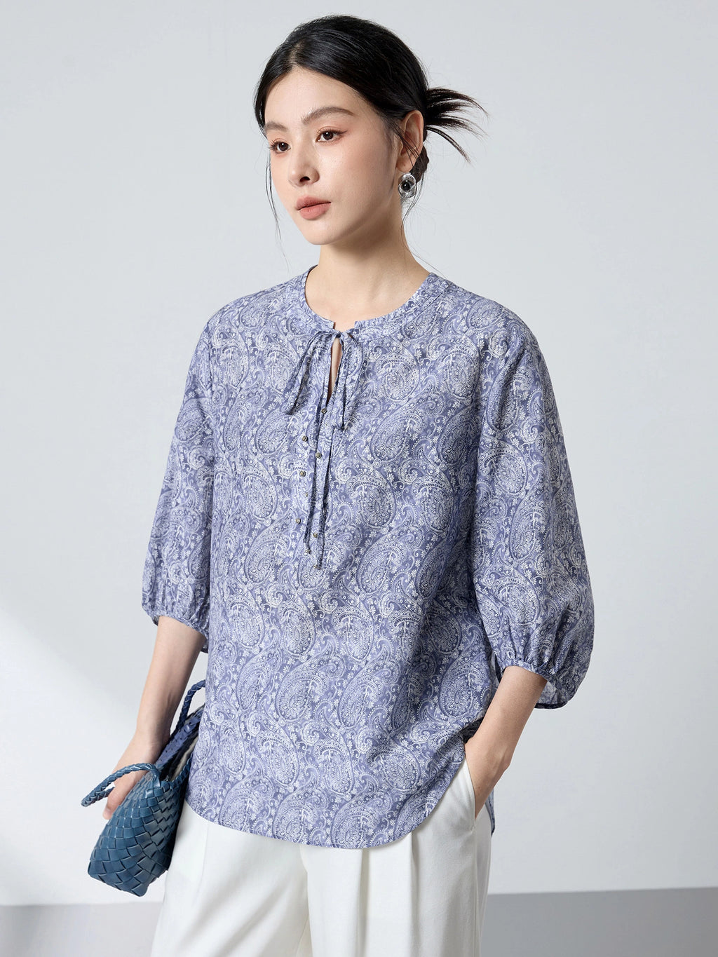 Side view of a women's blue paisley print blouse with lantern sleeves and a comfortable A-line fit, paired with white trousers.