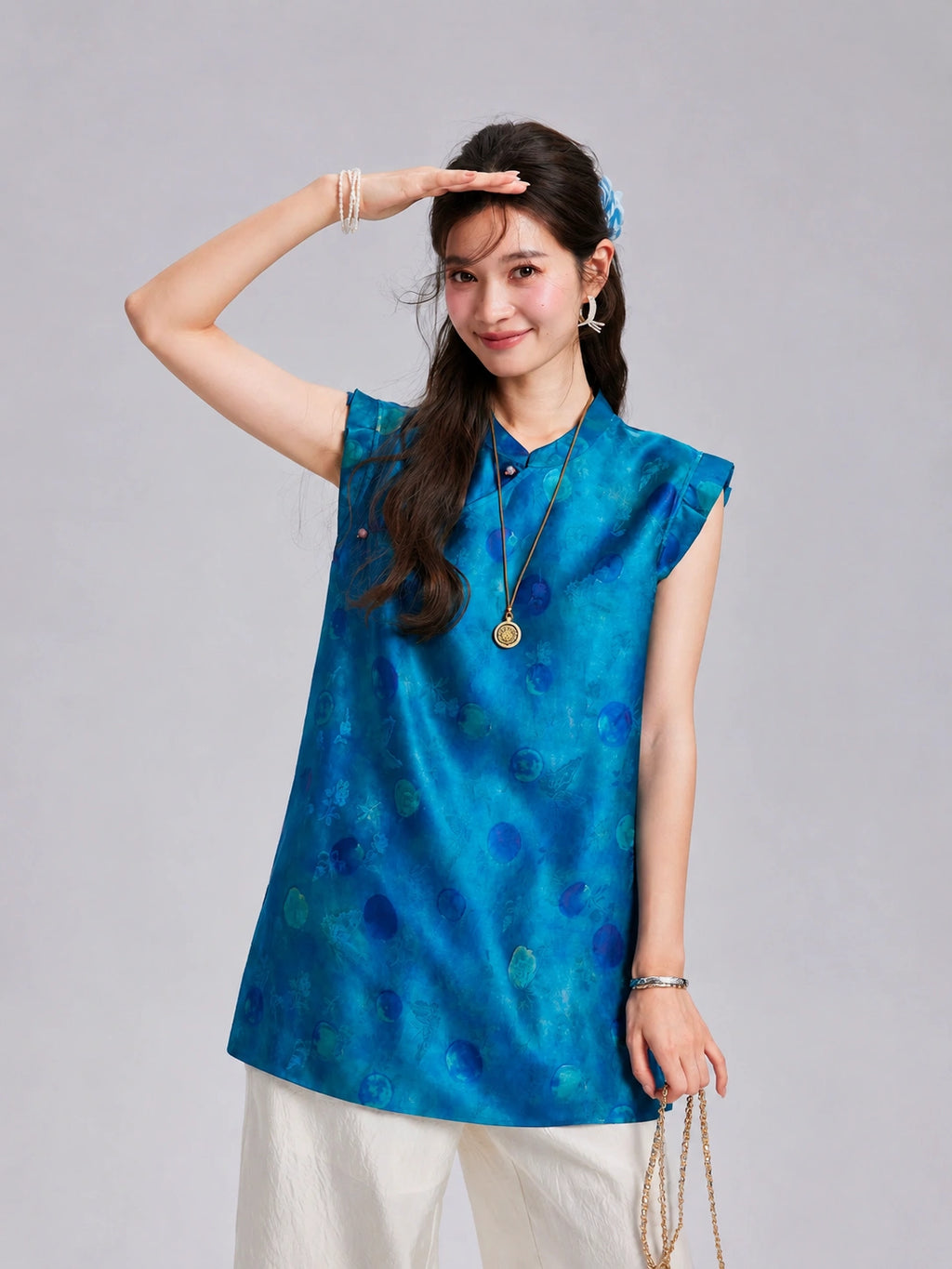 Close front view of a blue polka dot silk top with ruffled shoulders and button detail