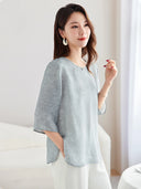 Model wearing a light blue silk-blend New Chinese style top with a round neckline, paired with white trousers.