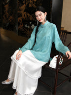 Seated model wearing a loose blue silk Mandarin collar shirt with long sleeves and bird flower jacquard texture
