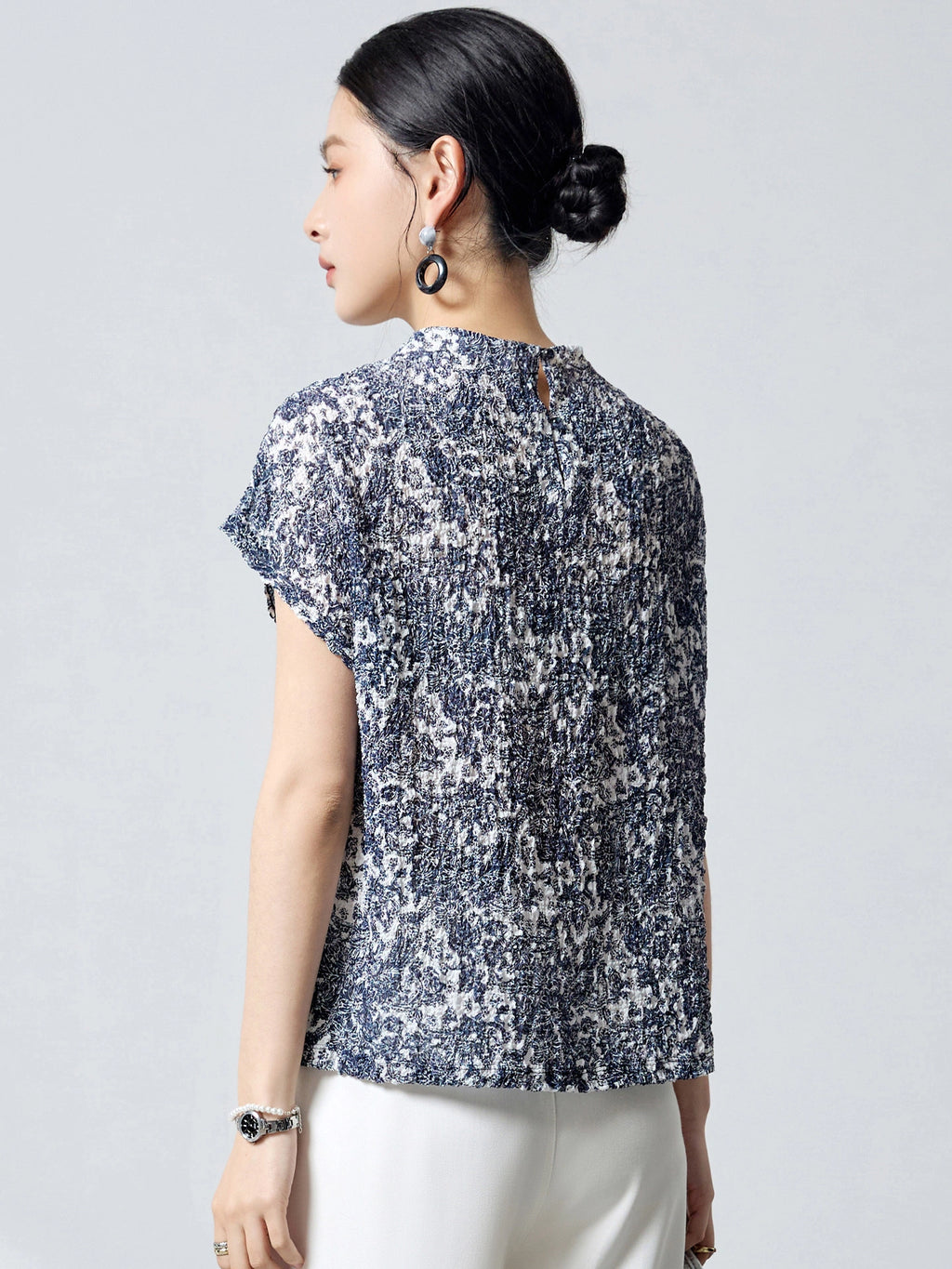 Back view of a blue and white printed silk top with a round neckline and a back keyhole button closure, crafted from 96.2% Mulberry Silk with bubble crepe texture.