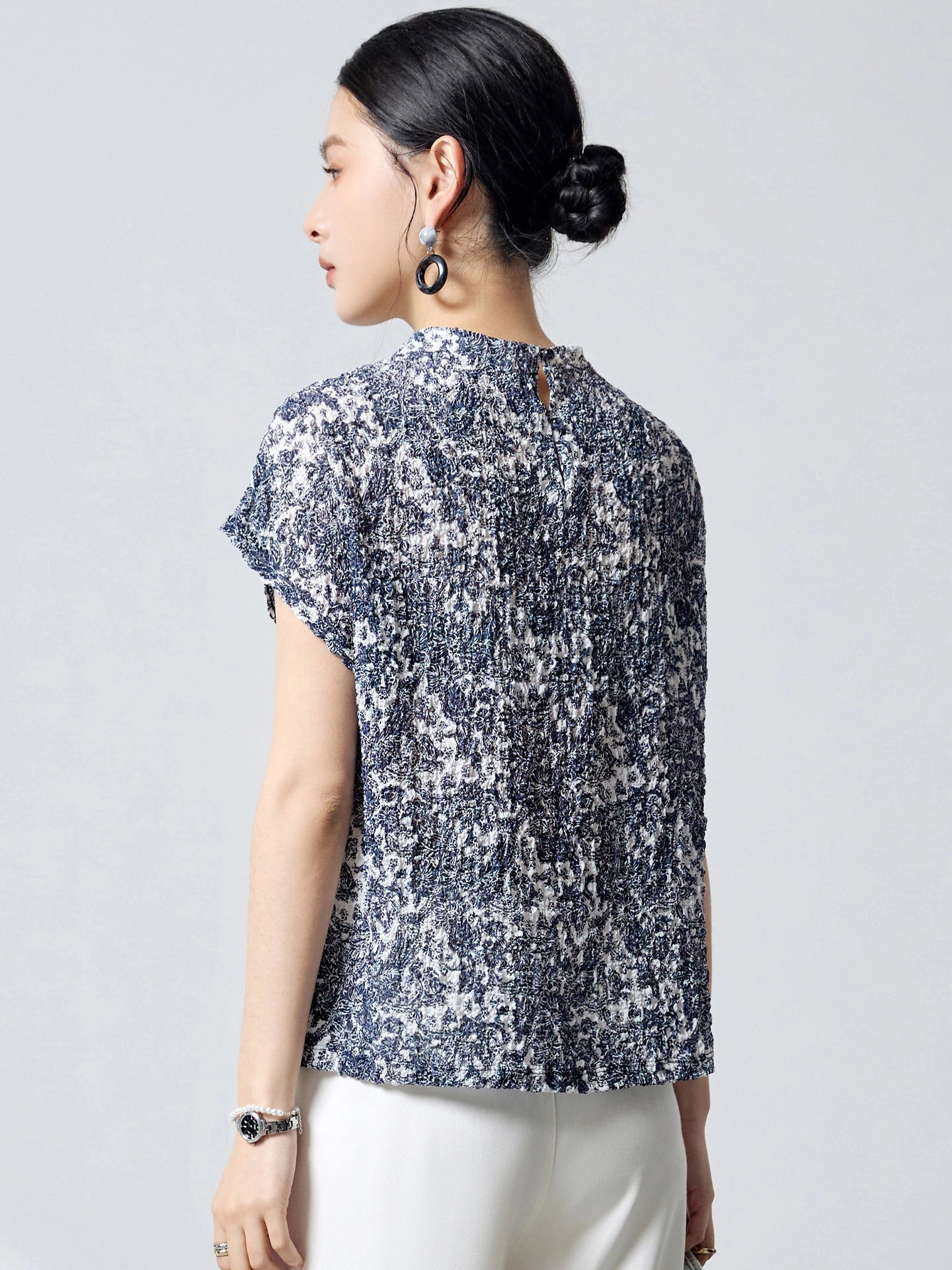 Back view of a blue and white printed silk top with a round neckline and a back keyhole button closure, crafted from 96.2% Mulberry Silk with bubble crepe texture.