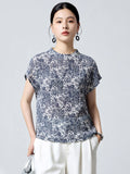 Front view of a women's blue and white printed silk blouse with short sleeves and a relaxed fit, paired with white trousers.