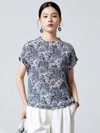 Front view of a women's blue and white printed silk blouse with short sleeves and a relaxed fit, paired with white trousers.