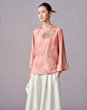 Woman wearing a blush pink jacquard blouse with floral embroidery and asymmetric buttons