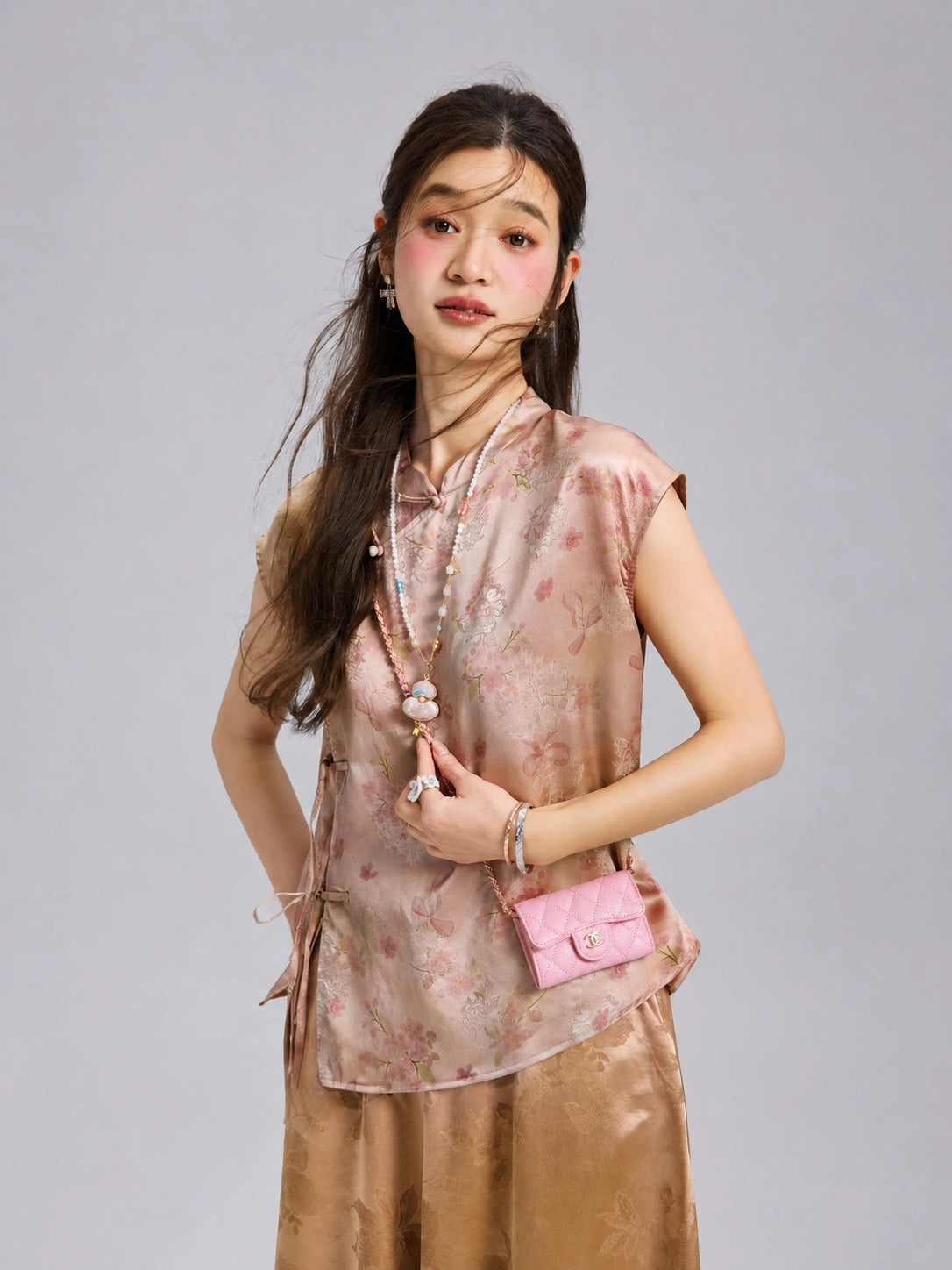 Three-quarter view of a woman wearing a blush floral Xiangyunsha silk top with traditional-inspired closures