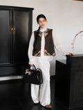 Model wearing a brown and gold Chinese-style silk vest with white trousers and a flowing contemporary look.