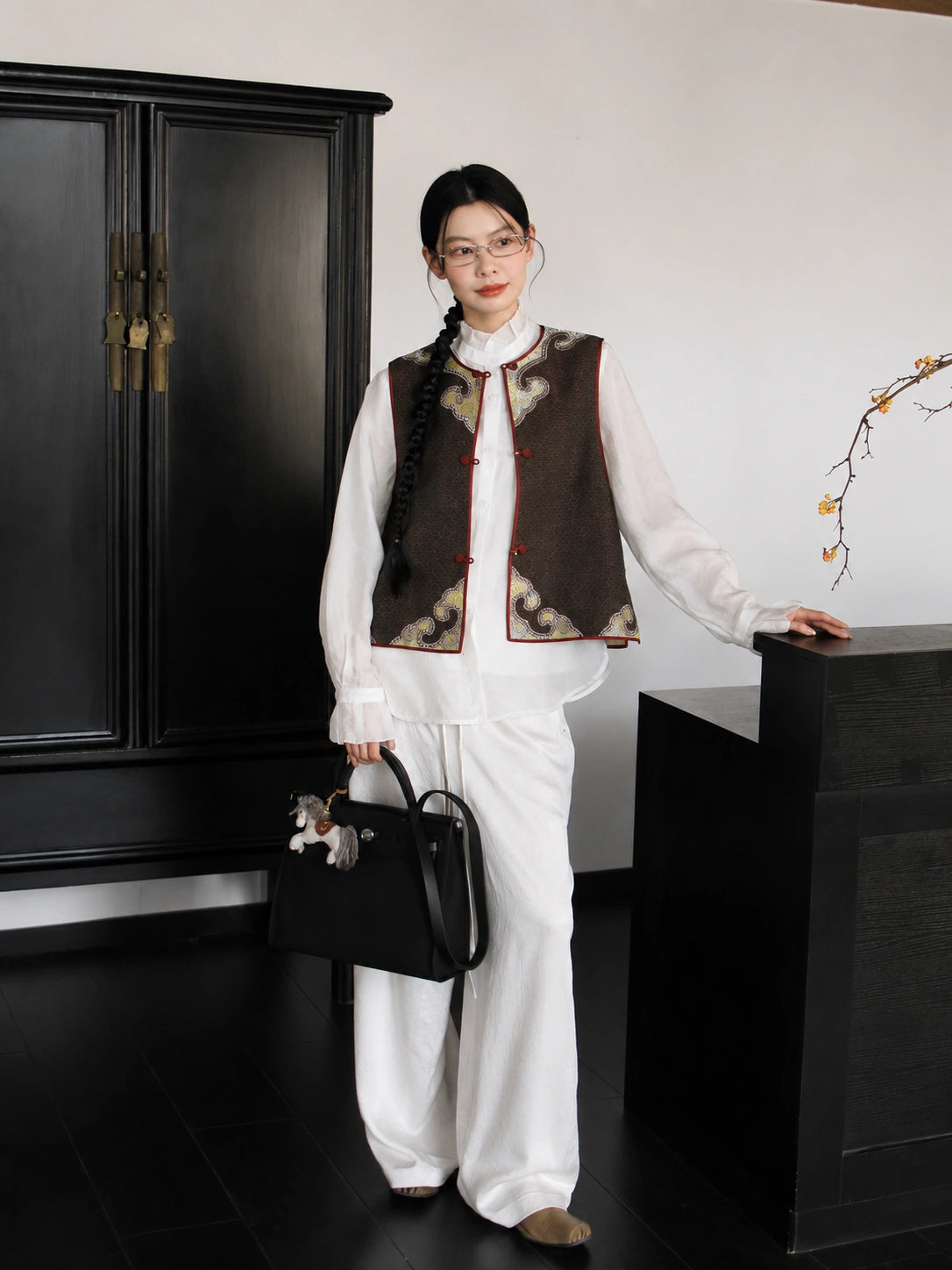 Model wearing a brown and gold Chinese-style silk vest with white trousers and a flowing contemporary look.