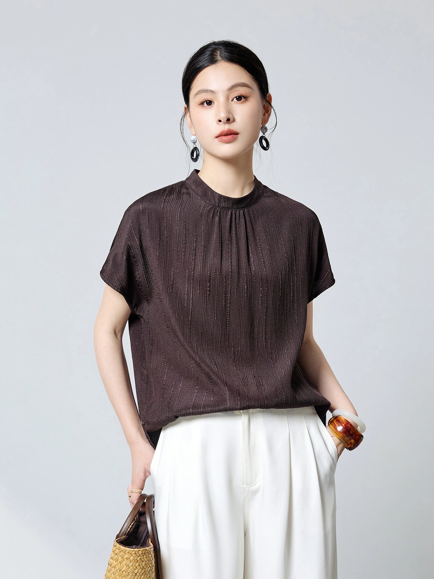 Front view of a dark brown textured silk blouse with a stand collar and short sleeves, styled with white wide-leg trousers, perfect for a chic commuter style.