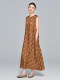 Model wearing a caramel brown 95%+ mulberry silk sleeveless dress with a round neckline and intricate geometric floral print, standing with hands in pockets.
