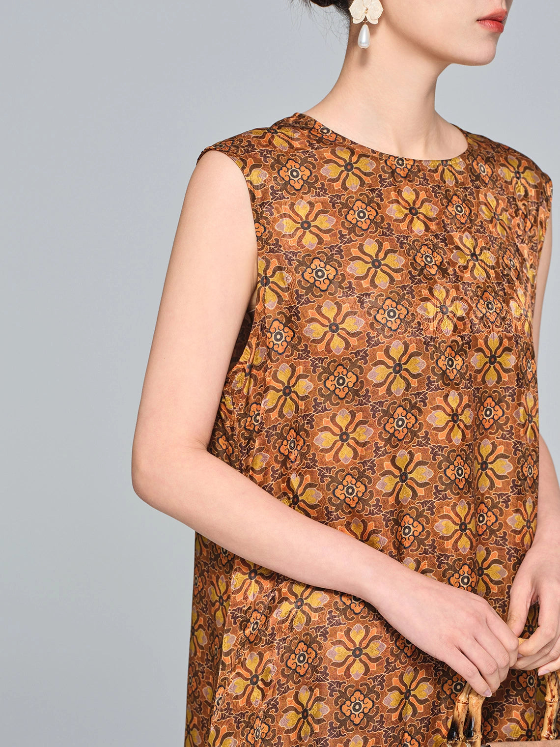 Side profile of a women's brown silk dress showing the sleeveless design, round neckline, and intricate batik-style print.