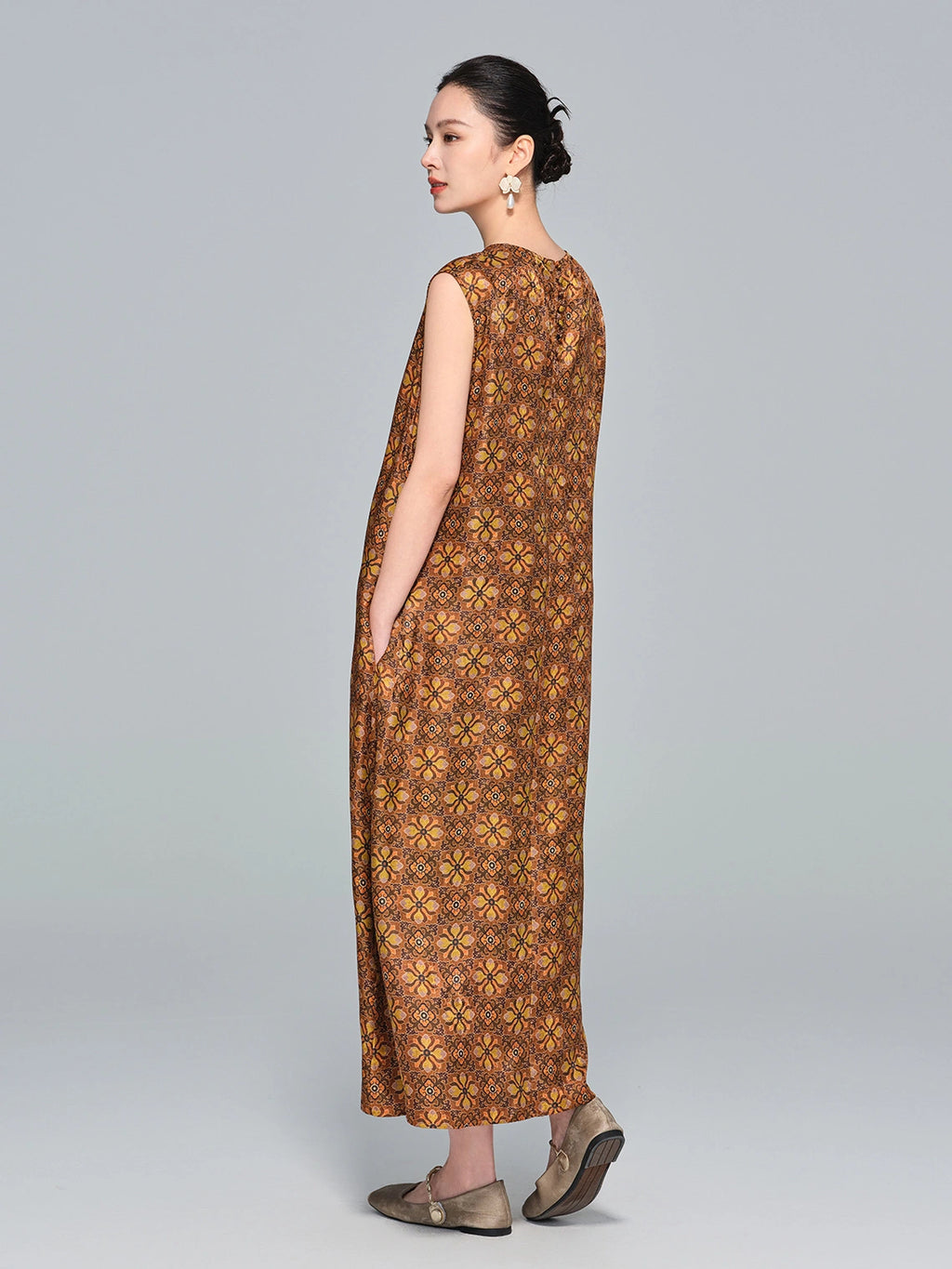 Side view of a brown silk sleeveless A-line dress with a round neckline, relaxed fit, and side pockets, paired with flat shoes.