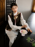Model wearing a brown Songjin silk Chinese vest with gold woven detailing over a white blouse.