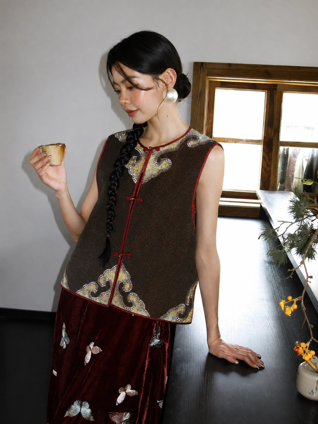 Close styling view of a brown mulberry silk vest with burgundy trim and ornate gold woven accents.