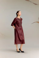 Side profile of a women's burgundy silk midi dress with a relaxed fit, three-quarter sleeves, and embroidered cuffs, styled with black heels for an elegant look.