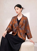 Seated model wearing the floral silk jacket with a black skirt