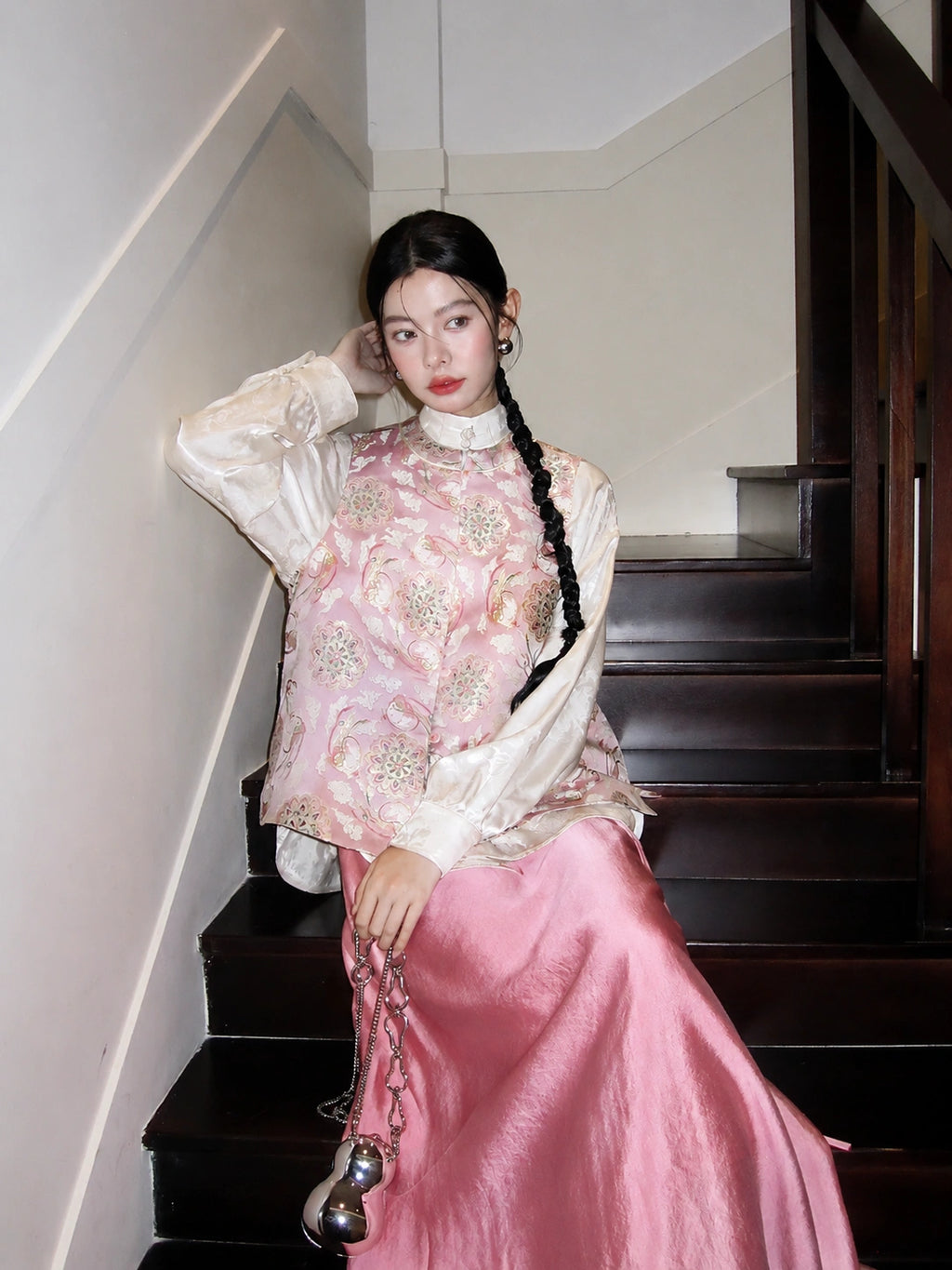 Seated model wearing the pink Jade Rabbit Song brocade silk vest layered over an ivory blouse
