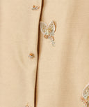 Close-up of a beaded butterfly motif and decorative button on champagne beige fabric