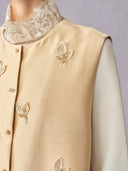 Close-up of the round neckline, butterfly embroidery and shoulder finish of the beige vest