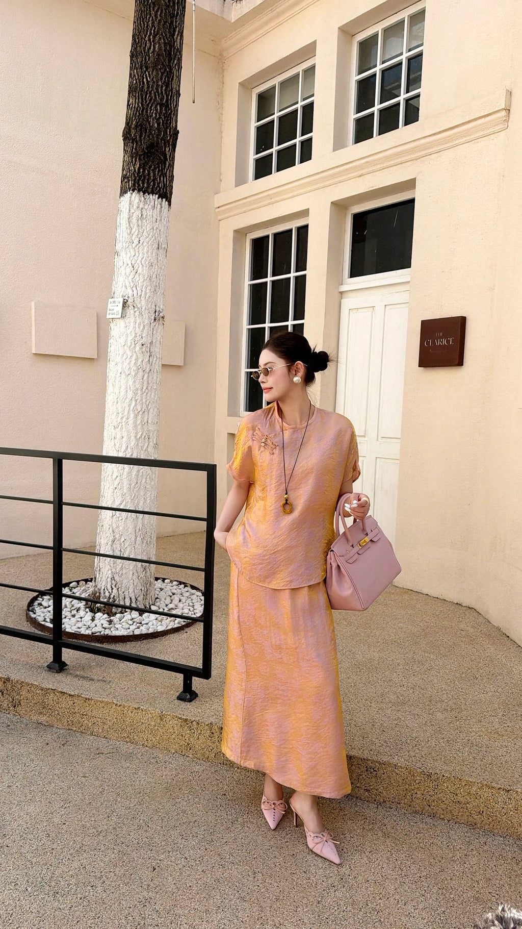 Model wearing a soft pink short sleeve Cheongsam top and matching midi skirt, holding a pink bag, perfect for elegant summer styling.