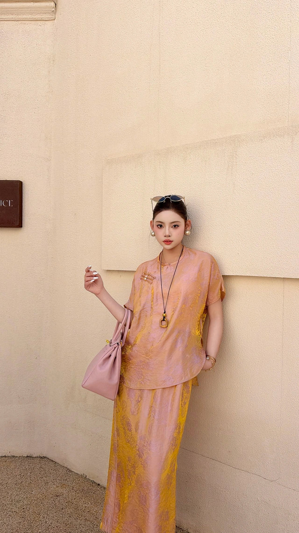 Full body shot of a viscose blend Cheongsam set in champagne rose, featuring a buttoned top and flowy side-slit skirt, paired with nude heels.