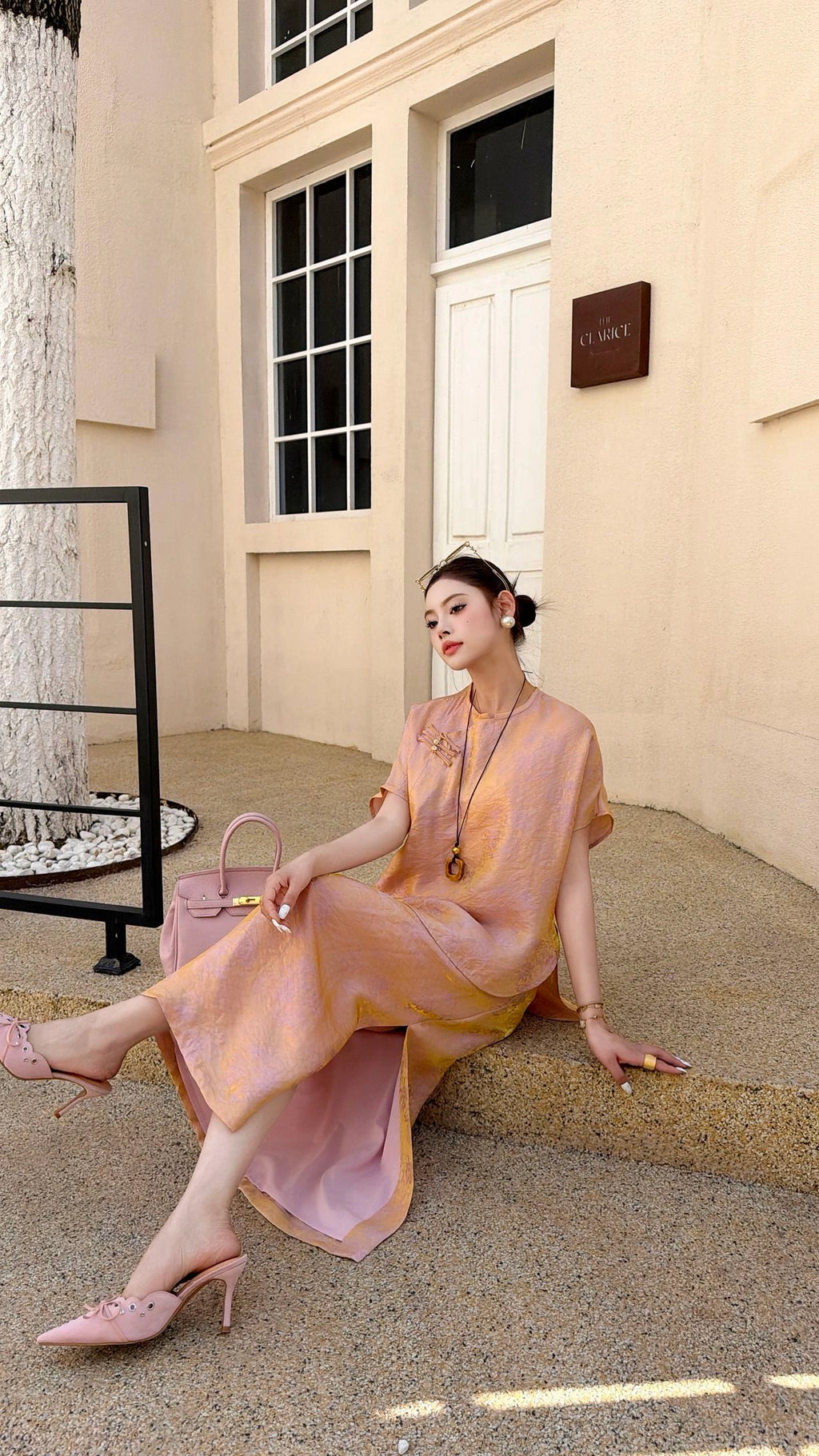 Sitting woman wearing a pink Cheongsam blouse and matching skirt, showcasing the comfortable fit and elegant drape of the 80% viscose, 20% nylon fabric.