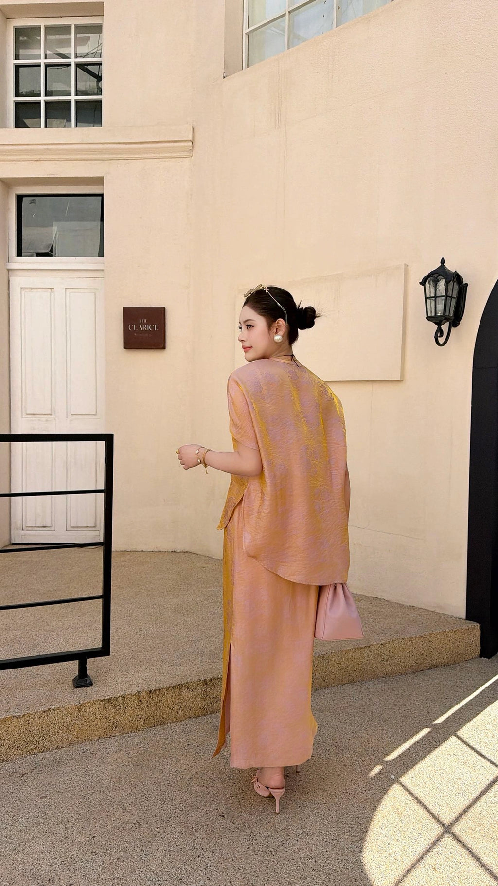 Back view of a champagne pink Cheongsam co-ord set with short sleeve top and side slit skirt, crafted from 80% viscose and 20% nylon, paired with pink heels.