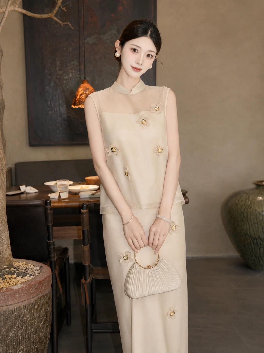 Model wearing a champagne Cheongsam set with sheer yoke and 3D floral appliqués, holding a pleated handbag, crafted from a Lyocell-Tencel blend.