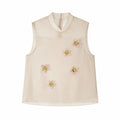 Flat lay of a champagne sleeveless Cheongsam top with a sheer yoke, back zipper, and scattered 3D floral appliqués, 90% Lyocell, 10% Polyester.