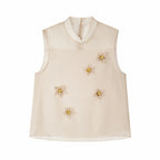 Flat lay of a champagne sleeveless Cheongsam top with a sheer yoke, back zipper, and scattered 3D floral appliqués, 90% Lyocell, 10% Polyester.