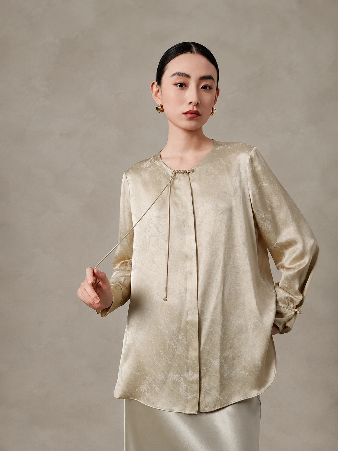 Front view of a champagne silk blend blouse with tie neckline