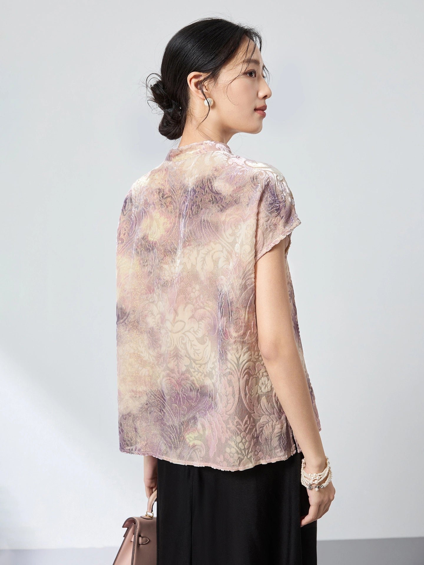 Back view of a champagne jacquard top with a stand collar and cap sleeves, featuring an abstract watercolor print, paired with a black skirt.