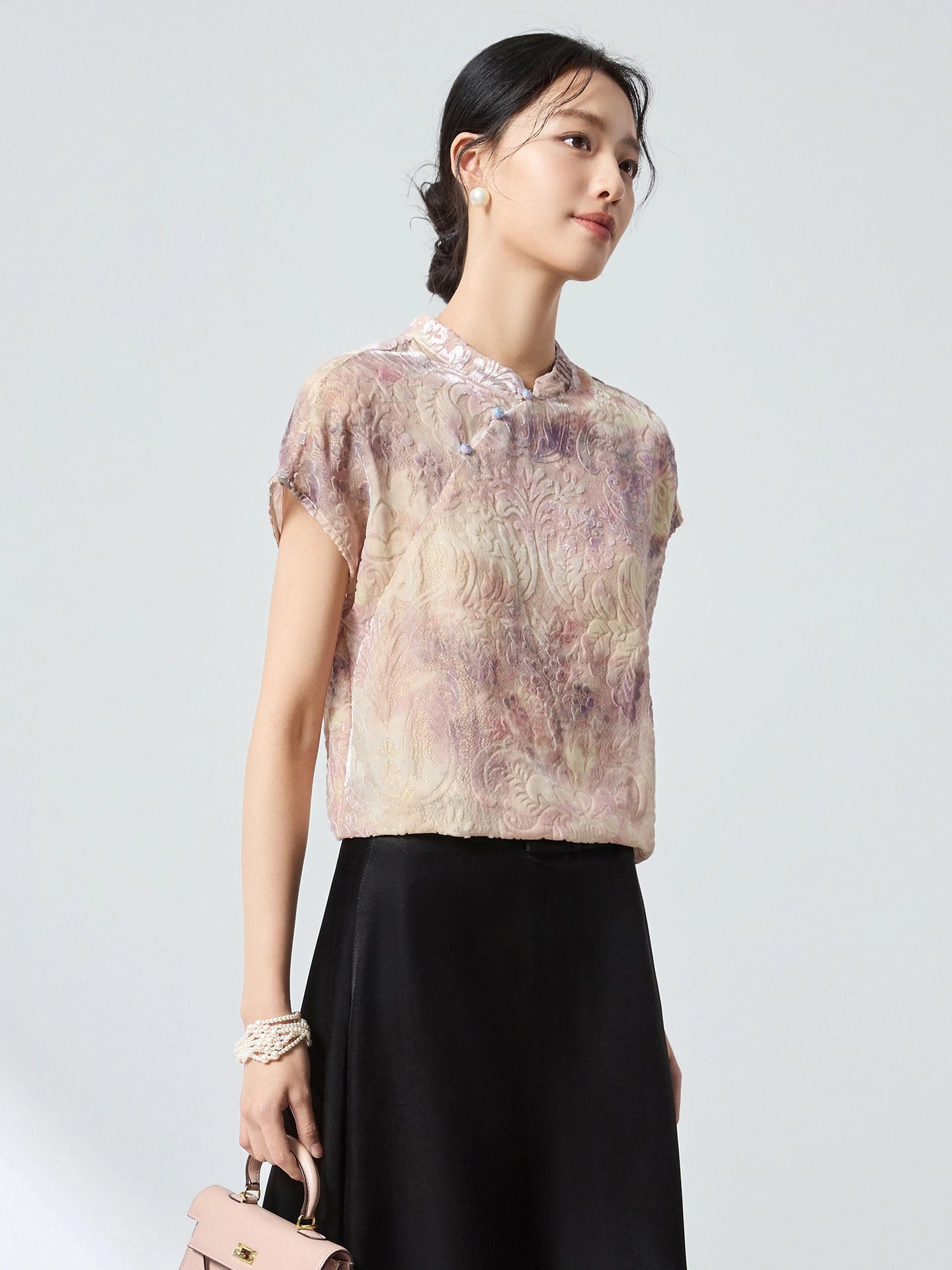 Model wearing a champagne jacquard top with a stand collar and cap sleeves, holding a pink handbag, highlighting the intricate pattern and soft sheen.