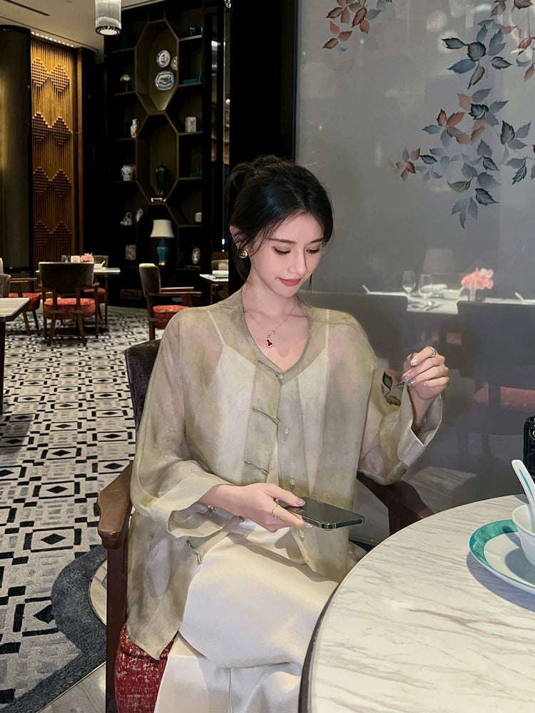 Woman seated in a Champagne Sage pure silk sheer cardigan styled over an ivory dress for an elegant layered look.