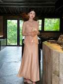 Model standing outdoors in a champagne satin maxi skirt, holding a pink handbag, crafted from 100% polyester, showcasing the versatility of the skirt.