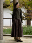 Full-length outfit with a charcoal olive stand-collar blouse, a long brown textured skirt and black shoes.