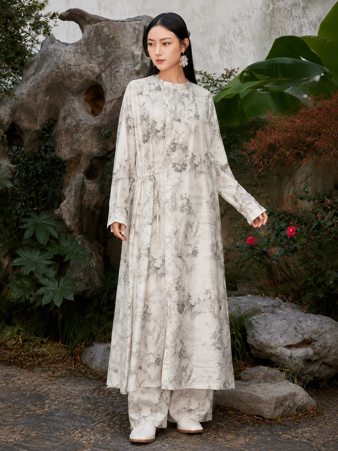 Side angle view of an ivory Chinese ink landscape print maxi dress featuring a relaxed silhouette, long sleeves and adjustable side tie waist.