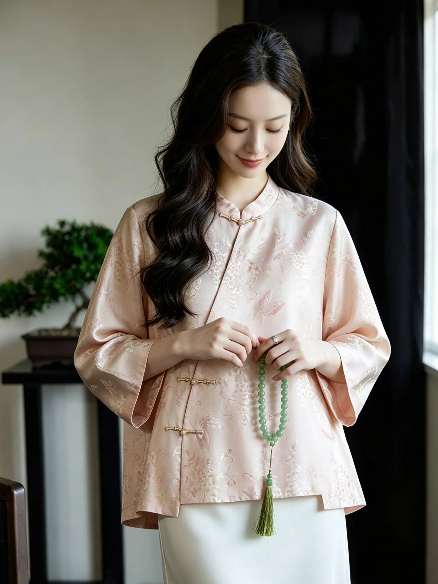 Chinese-inspired blush pink jacquard silk blouse styled with white trousers and green accessories