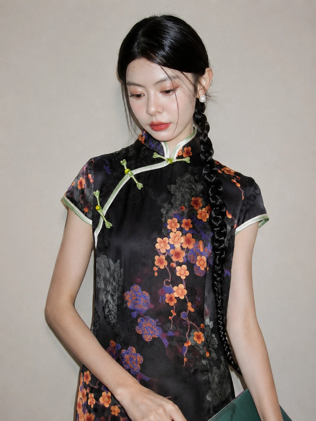 Upper-body close-up of a black floral rayon jacquard qipao with diagonal front closure, mandarin collar, and green piping.