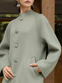 Close-up of the sage green coat showing its textured fabric, stand collar, covered buttons, and slanted pocket