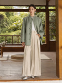 Sage green Chulan coat worn partially open over a white top and cream pleated wide-leg trousers