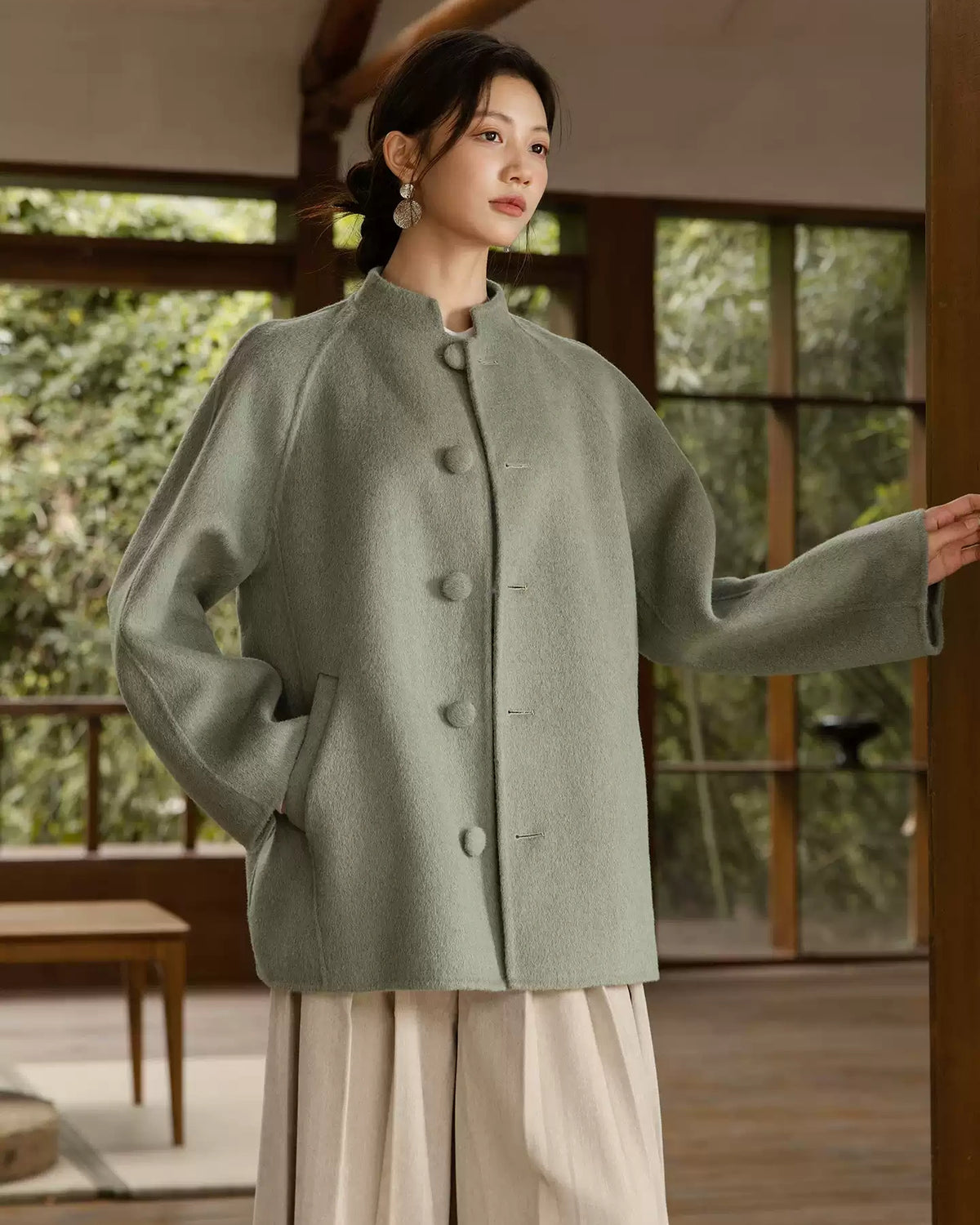 Sage green coat with one arm extended, showing the raglan sleeves and matching covered buttons