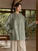 Sage green coat with one arm extended, showing the raglan sleeves and matching covered buttons
