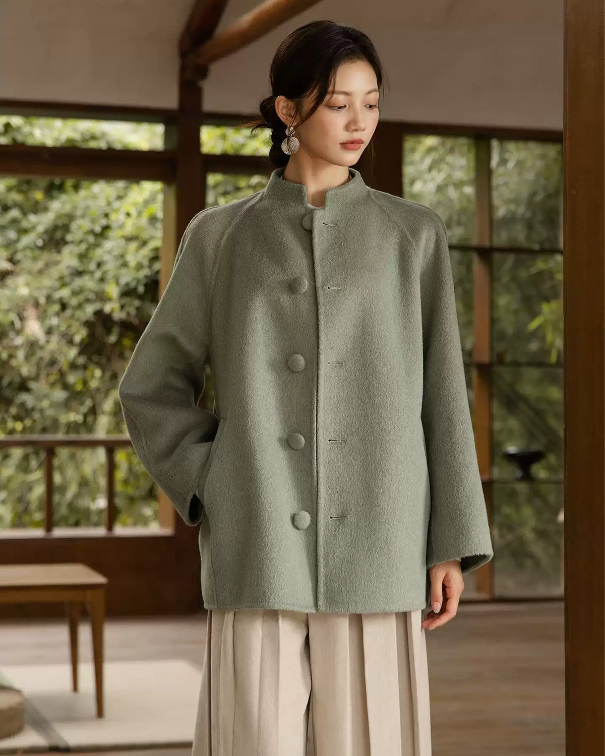 Front view of the sage green Chulan coat showing its stand collar, fabric-covered buttons, and slanted pocket