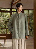 Front view of the sage green Chulan coat showing its stand collar, fabric-covered buttons, and slanted pocket