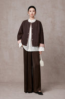 Model wearing the cocoa-brown jacket with pink cuffs over a white shirt and wide-leg trousers