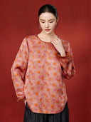 Model wearing the coral pink silk blouse with orange geometric blocks, floral outlines and brown textured cuffs.