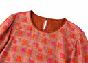Close-up of the coral pink blouse’s round neckline, orange binding and geometric floral print.