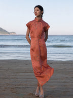 Woman wearing a Chinese style silk blend maxi dress in Coral Sunset with a mandarin collar and cap sleeves by the beach.