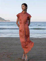 Woman wearing a Chinese style silk blend maxi dress in Coral Sunset with a mandarin collar and cap sleeves by the beach.